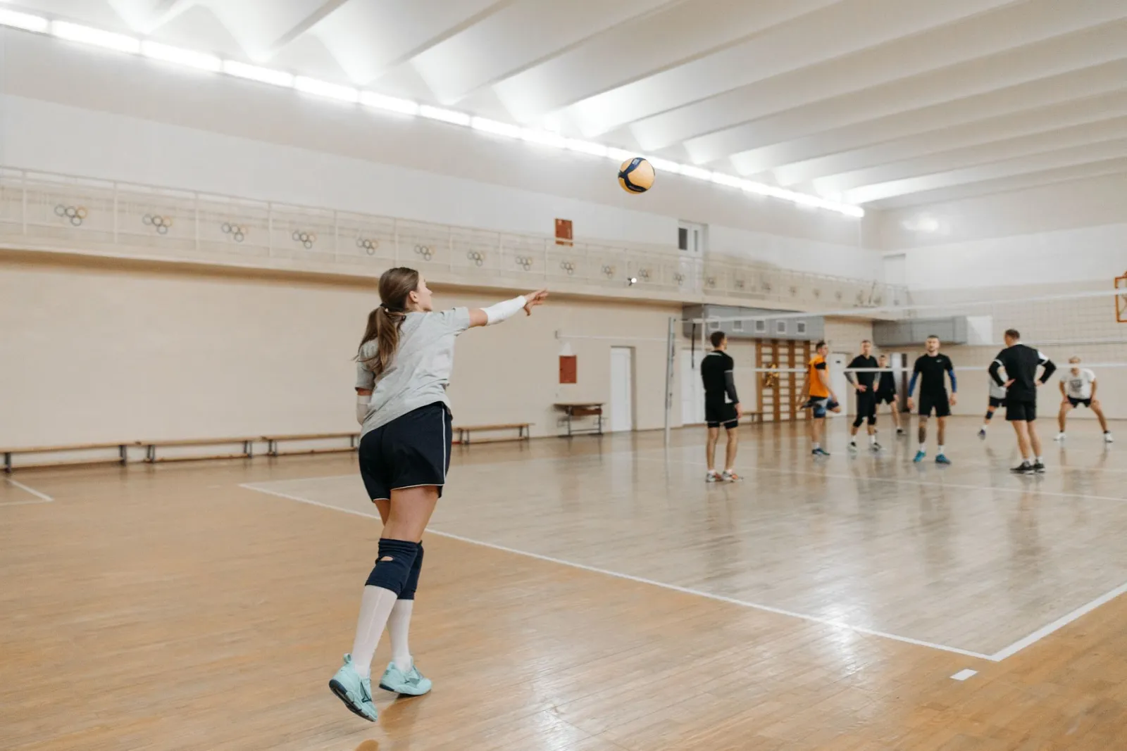 Athletes practicing volleyball indoors, focusing on gameplay strategy.