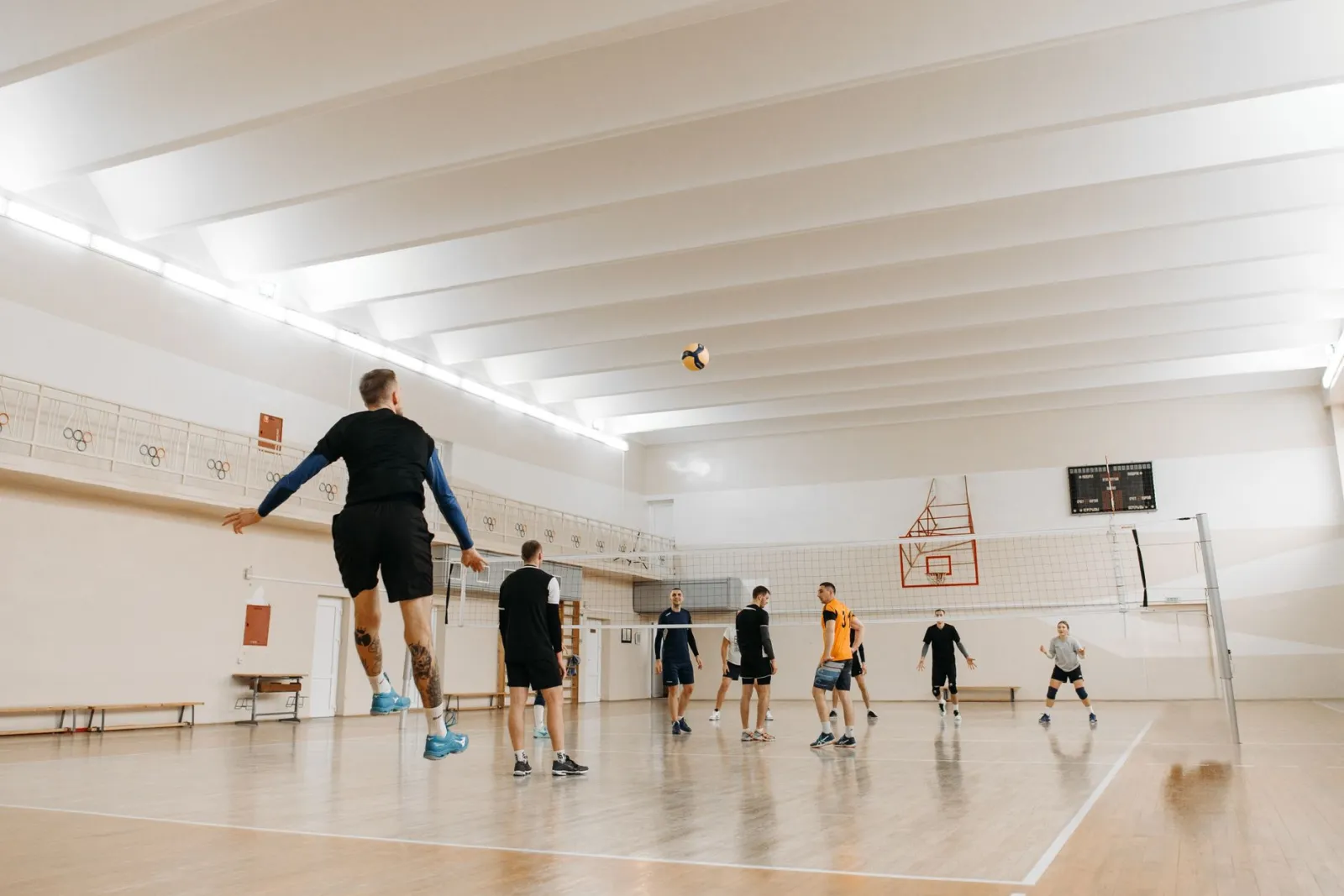 A dynamic indoor volleyball match featuring six athletes jumping and playing vigorously.